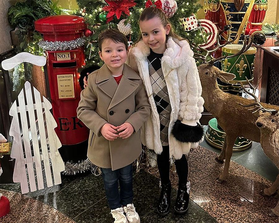 Two smartly dressed kids smiling surrounded by Christmas decorations